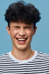 smiling man with curly hair wearing striped shirt laughs joyfully with closed eyes against light...