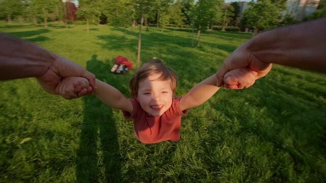 First-person view, father holding his son's hands, spinning him around in a circle at the park, joyful child laughs, enjoying the playful moment, creating happy childhood and family memories together