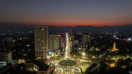 Aerial night views of a brightly illuminated central roundabout and surrounding cityscape in Thai...