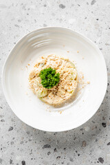 A white plate with a creamy salad, garnished with fresh parsley and crushed nuts, sits on a speckled gray surface. A simple and elegant presentation highlighting fresh ingredients.