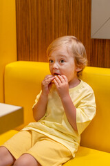 Young child wearing a yellow clothes eats a cheeseburger in a vibrant restaurant, enjoying fast food meal in a casual dining environment. Kids diet, bad food choices, early junk food addiction