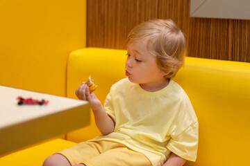 A small child wearing a yellow shirt is eating chicken nuggets in a vibrant environment. Four year old boy enjoying fast food meal. Kids diet, bad food choices, early junk food addiction
