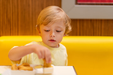 A small child wearing a yellow shirt is eating chicken nuggets in a vibrant environment. Four year old boy enjoying fast food meal. Kids diet, bad food choices, early junk food addiction
