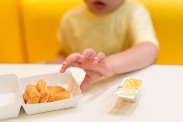 A small child wearing a yellow shirt is eating chicken nuggets in a vibrant environment. Four year old boy enjoying fast food meal. Kids diet, bad food choices, early junk food addiction