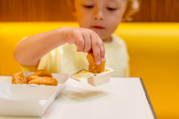 A small child wearing a yellow shirt is eating chicken nuggets in a vibrant environment. Four year old boy enjoying fast food meal. Kids diet, bad food choices, early junk food addiction