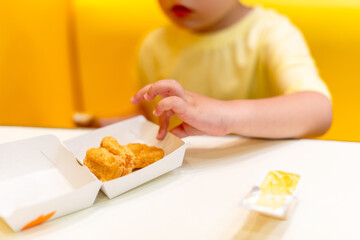 A small child wearing a yellow shirt is eating chicken nuggets in a vibrant environment. Four year old boy enjoying fast food meal. Kids diet, bad food choices, early junk food addiction