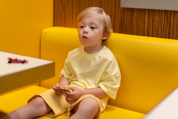 Young child wearing a yellow clothes eats a cheeseburger in a vibrant restaurant, enjoying fast food meal in a casual dining environment. Kids diet, bad food choices, early junk food addiction
