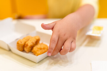 A small child wearing a yellow shirt is eating chicken nuggets in a vibrant environment. Four year old boy enjoying fast food meal. Kids diet, bad food choices, early junk food addiction