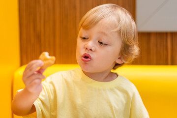A small child wearing a yellow shirt is eating chicken nuggets in a vibrant environment. Four year old boy enjoying fast food meal. Kids diet, bad food choices, early junk food addiction