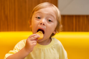 A small child wearing a yellow shirt is eating chicken nuggets in a vibrant environment. Four year old boy enjoying fast food meal. Kids diet, bad food choices, early junk food addiction