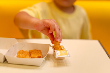 A small child wearing a yellow shirt is eating chicken nuggets in a vibrant environment. Four year old boy enjoying fast food meal. Kids diet, bad food choices, early junk food addiction
