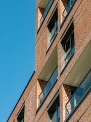 Contemporary brick apartment facade with glass balconies under clear blue sky in South Spain, ideal...