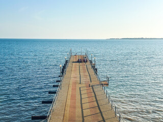Symmetrical view of long pier stretching into sea under clear sky, perfect for themes of travel, solitude, symmetry, and calm seascapes
