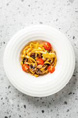 A plate of pasta with mushrooms and cherry tomatoes, served on a white dish against a speckled grey background. The vibrant colors and appetizing presentation highlight the fresh ingredients.