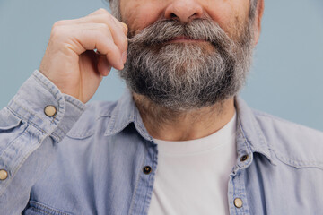 Obraz premium Senior man twisting his gray mustache on blue background