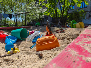 A pile of toys and a toy car are on the sand. The toys are scattered and the car is in the middle of the pile. The scene is messy and disorganized