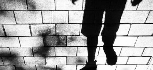 Silhouette shadow of a person legs, walking toward on city street sidewalk in black and white