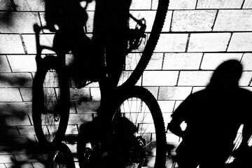 Shadow silhouette of cyclist and pedestrian on city sidewalk traffic, in black and white high contrast