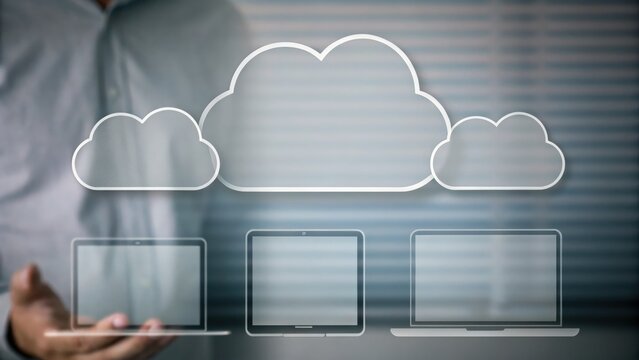 Businessperson presenting digital cloud computing concept with three laptops and cloud icons.