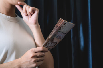 A person is holding a stack of bills in their hand. The person appears to be deep in thought,...