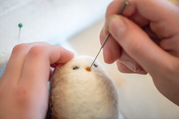 Close-up of artist's hands using a special needle to create a needle felted animal toy from wool roving, demonstrating the delicate process of needle felting