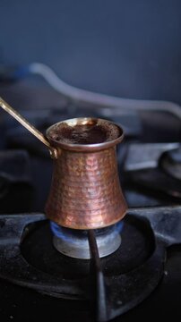An authentic and artisanal mood is captured as a hand carefully holds a traditional hammered copper cezve pot directly over a blue gas flame