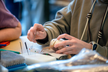 Close-up of a student's hands meticulously shaping a small animal figurine using needle felting techniques during a crafting workshop, surrounded by tools and materials