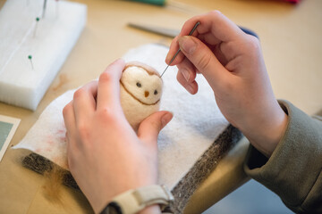 Close-up of artist's hands using a special needle to create a needle felted animal toy from wool roving, demonstrating the delicate process of needle felting