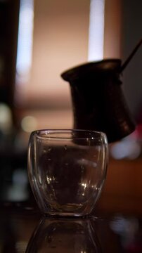 An inviting and sensory mood is captured as dark, hot coffee is poured from a ladle into a sleek double-walled glass, with steam rising
