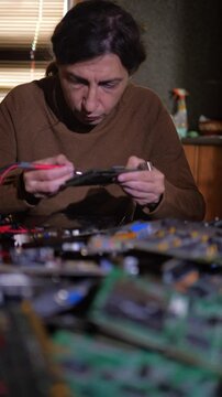 A focused and technical mood is captured as a person uses a multimeter to test components on a circuit board, with other electronics blurred in the foreground