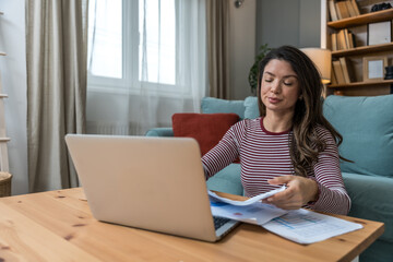 Young woman struggling with focus while working on laptop on floor, surrounded by printed analytic,...