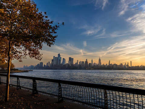 Wide view of the New York skyline at sunrise, with fall trees framing the shot from Hoboken on the New Jersey side.