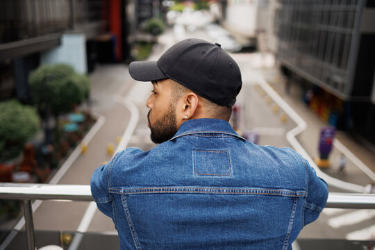 Back view of african american man in baseball cap standing near railing on street