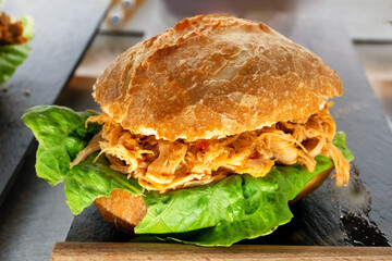 Hearty pulled pork sandwich with fresh lettuce on bun – street food snack at market in natural light