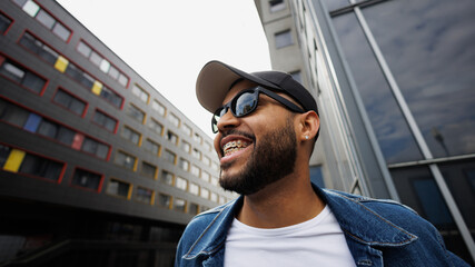 Cheerful african american man in sunglasses and baseball cap standing outdoors