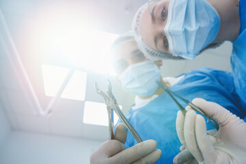 dentist surgeon holding teeth for tooth extraction with assistant leaning and looking at patient. ...