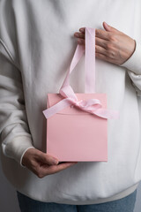 Pink box with pink ribbon in girl's hands. Space for text and logo. Gift wrapping