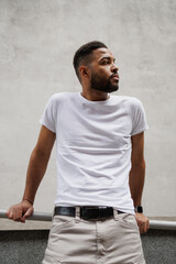 Bearded african american man in white t-shirt standing near railing on street