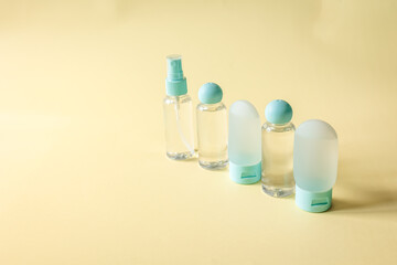 Minimalist flat lay of transparent travel bottles on pastel yellow background. Bright natural light and clean composition convey freshness and modern lifestyle