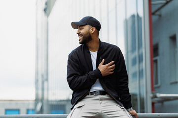 Smiling african american man in bomber jacket sitting on railing on street