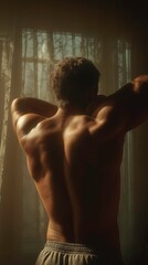 Muscular Man Stretching Shirtless in Dimly Lit Room with Backlit Window