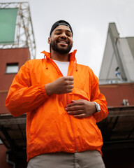 Smiling african american man in baseball cap zipping windbreaker on city street