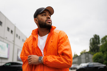 African american man in baseball cap and windbreaker looking away on street
