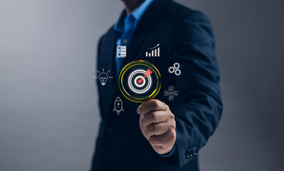 Concept of goals and objective ,Businessman hand holding magnifying glass show dartboard and arrow virtual icon for setting business goals, business plan, marketing, strategy or organization mission