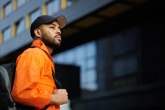 African american man in windbreaker and baseball cap holding backpack outdoors
