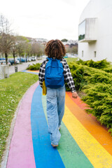 Young latin student with afro hair and backpack walking on rainbow crosswalk at university campus