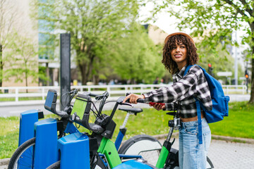 Obraz premium Young latin student renting a bike sharing service using her smartphone app, sustainable mobility concept