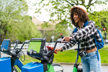 Young latin tourist unlocking a bike sharing in the city using her smartphone app, sustainable...