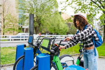 Young latin american student unlocking a shared bike in the city using a bike sharing service, promoting sustainable urban mobility