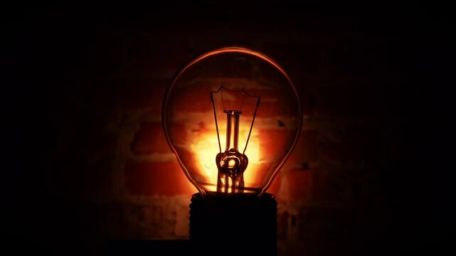 Tungsten light bulb lamp against brick wall in darkness.